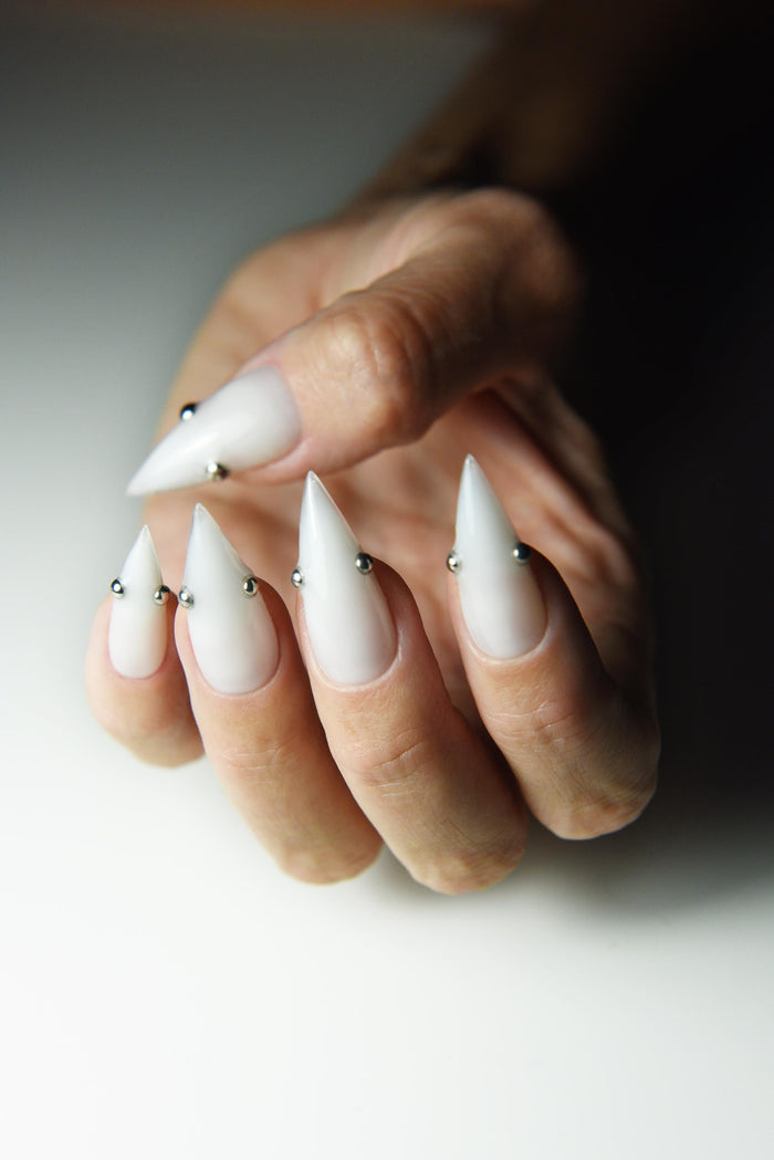 Milky white press-on nails with small metallic piercing studs – detail view