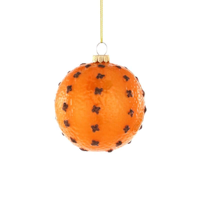 An orange Christmas ornament shaped like a whole orange, decorated with small dark cloves, hanging from a gold string against a plain white background.