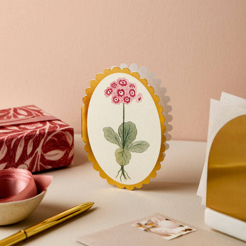 Decorative card with floral design on a table with gift wrap and pen.