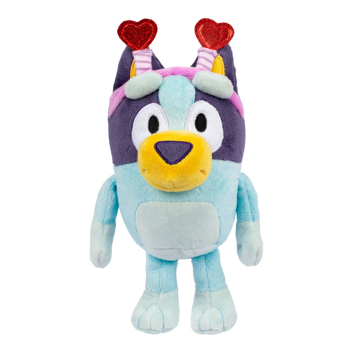 The Bluey & Friends Plushie by Moose Toys is a blue cartoon dog with a big yellow nose, dark blue ears, and light blue belly, wearing a headband with two red glittery hearts.
