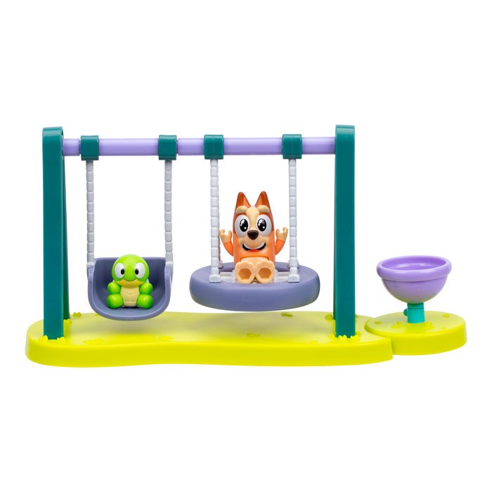 The Bluey Mini Playset & Figures by Moose Toys features a green and purple swing set with a green turtle figure and an orange cartoon dog. Ideal for fans of collectible playsets or your Bluey Mini-Figure Playset collection.