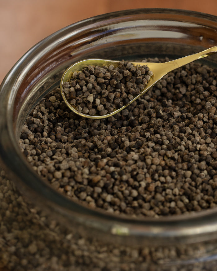 Glass jar filled with dark granular substance, with a gold spoon inside.