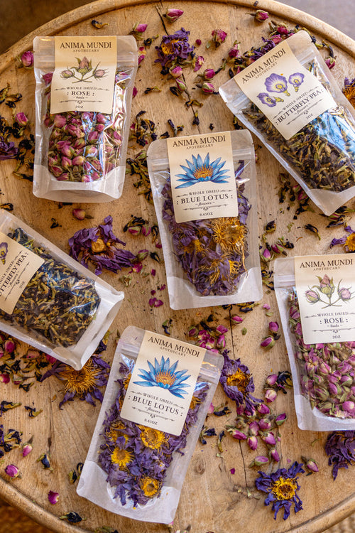 Anima Mundi tea packages on a wooden surface with dried flowers.