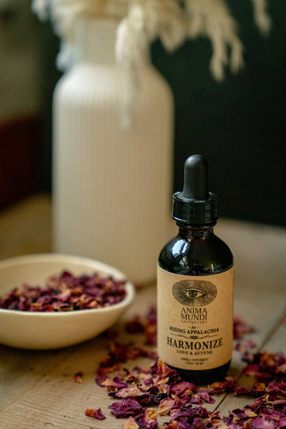 Bottle of Anima Mundi Harmonize on a wooden surface with dried flowers and a white vase in the background.