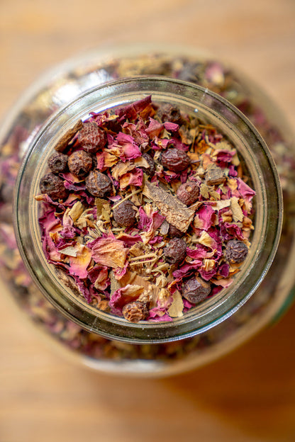 Close-up of a glass jar filled with dried flowers and herbs on a wooden surface.