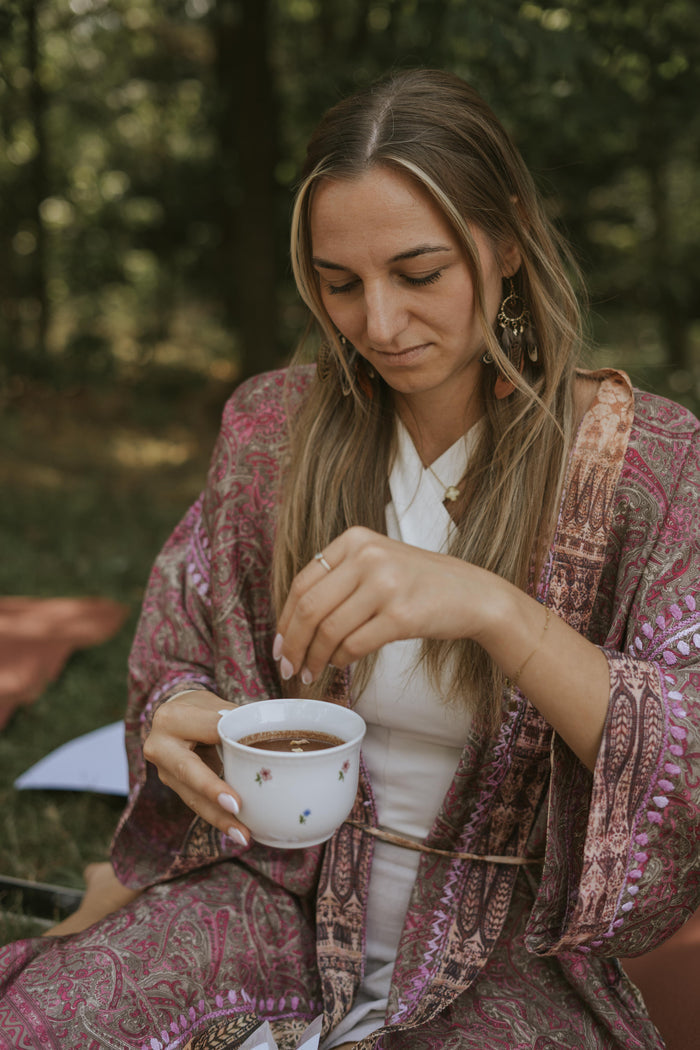 Woman in a patterned robe holding a cup outdoors