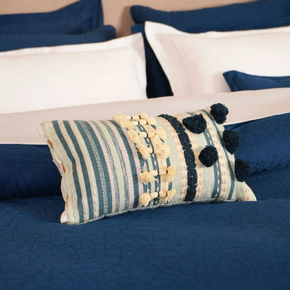 Blue quilted duvet cover with cream pillows and striped decorative pom-pom cushion