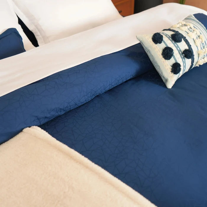 Blue quilted duvet cover with cream pillow and striped pom-pom cushion