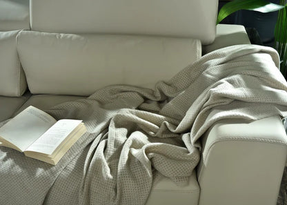Light brown knitted throw blanket with textured weave, draped over sofa arm.