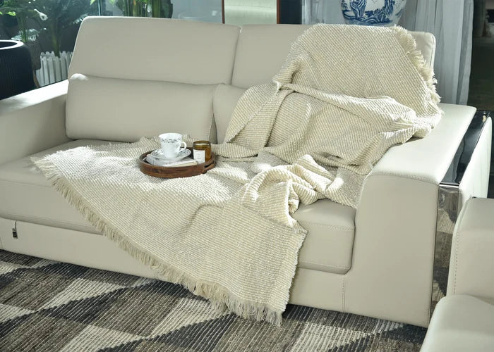 Light taupe knitted throw blanket with fringed edges, draped on couch