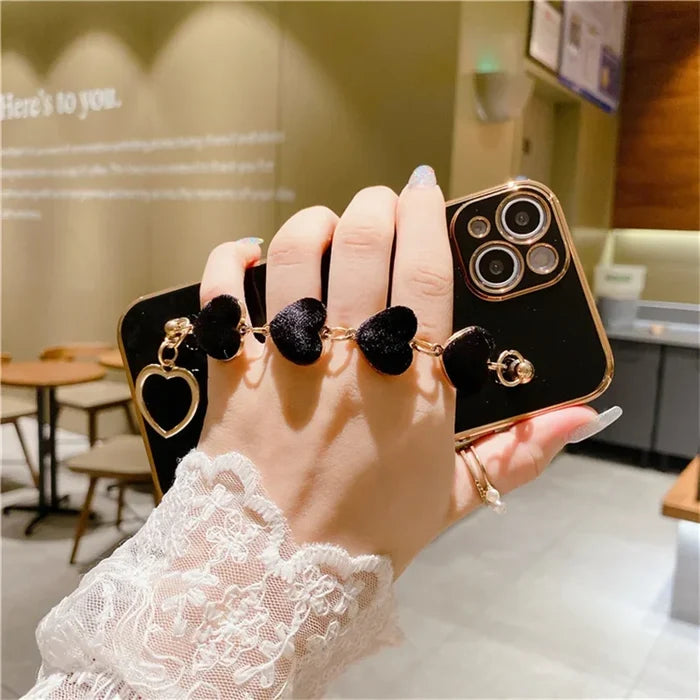 Decorative iPhone case with black heart-shaped charms attached to a wrist strap.