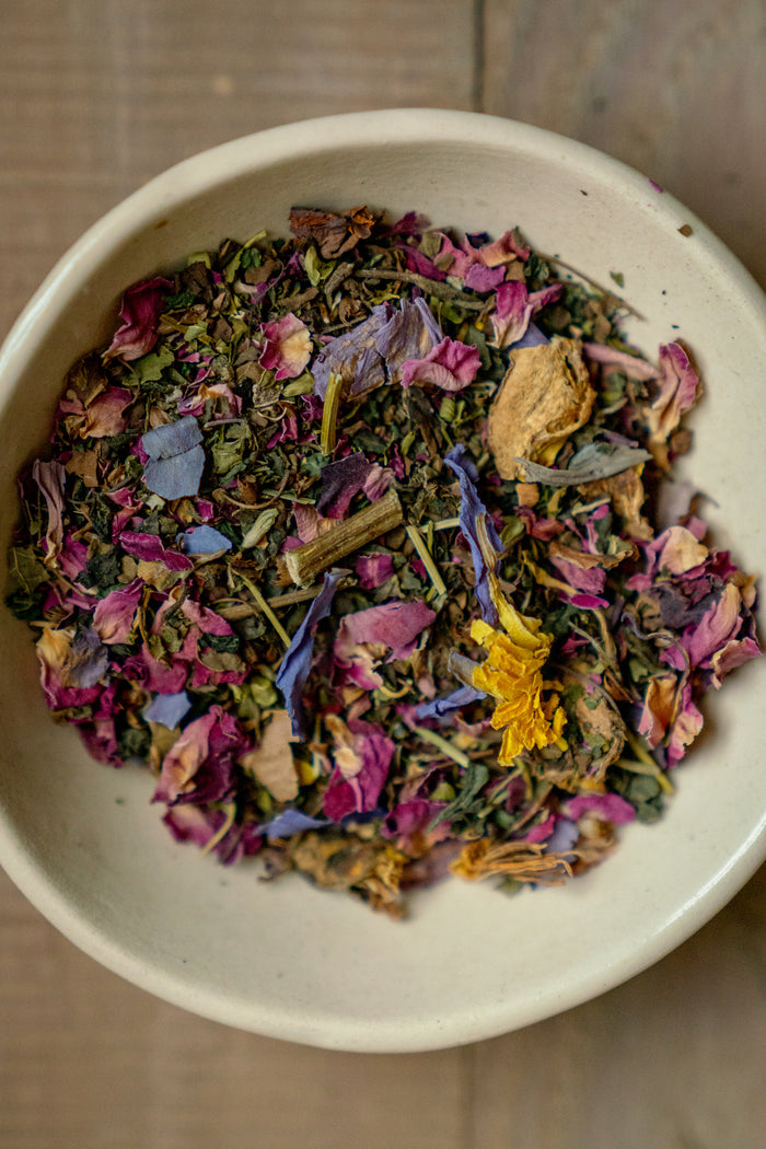 White bowl filled with a mix of dried herbs and flowers on a wooden surface
