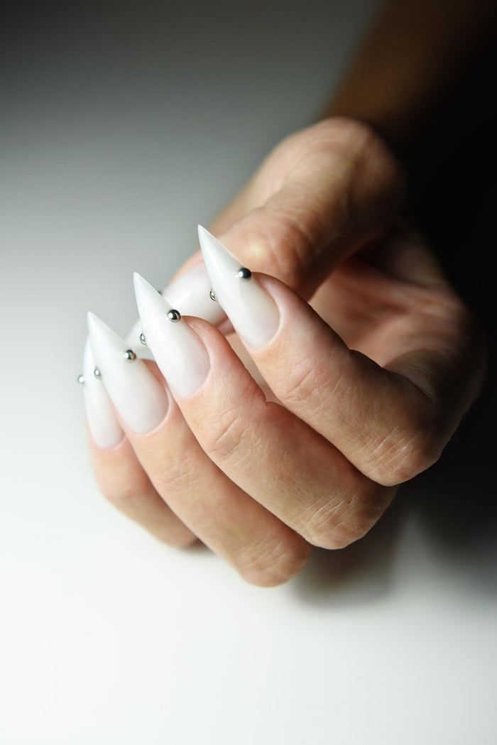Milky white press-on nails with small metallic piercing studs – detail view