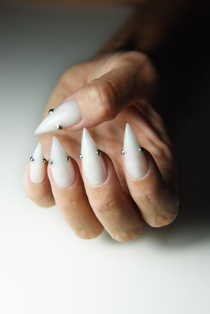 Milky white press-on nails with small metallic piercing studs – detail view