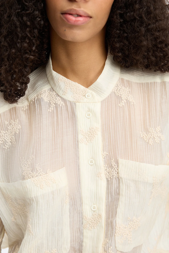 Close-up of a woman wearing the MUNTHE Fortunato Top Crème with delicate embroidery and button details, shop Munthe at Dotique.