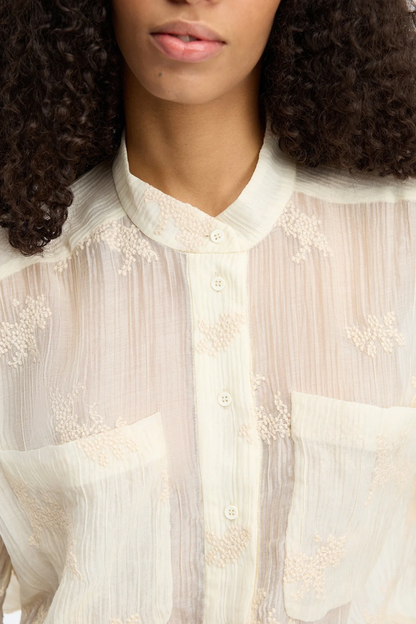 Close-up of a woman wearing the MUNTHE Fortunato Top Crème with delicate embroidery and button details, shop Munthe at Dotique.
