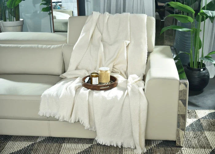 Natural knitted throw blanket draped over sofa, fringed edges