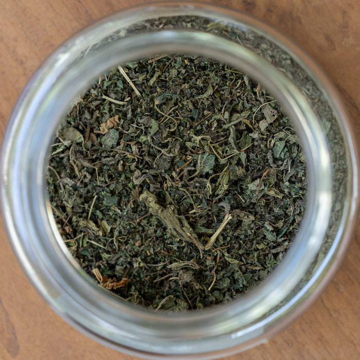 Close-up of a glass jar filled with dried green herbs on a wooden surface.