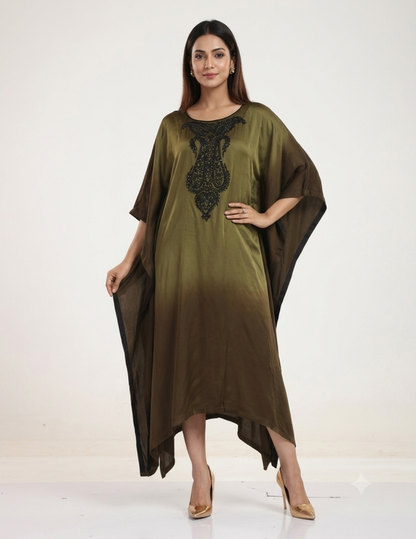 A female model standing against a neutral studio background, wearing an olive-to-brown ombre kaftan dress with intricate black bead embroidery on the neckline, paired with gold heels.