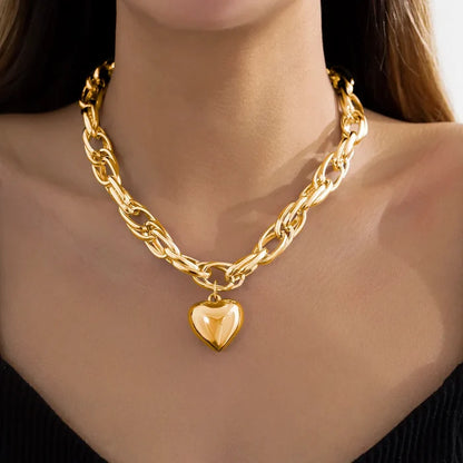 A person wearing a gold-colored oversized heart pendant necklace with a twisted chain design.