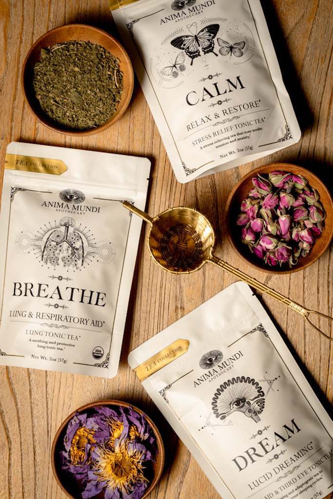 Anima Mundi tea packages labeled 'Calm', 'Breathe', and 'Dream' on a wooden surface with tea leaves and flowers.