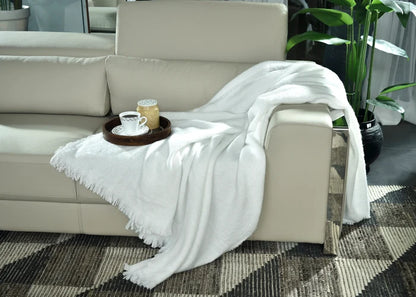 White knitted throw blanket with fringed edge, draped over sofa arm