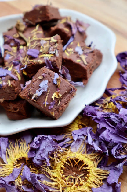 Chocolate fudge with dried flowers on a white plate surrounded by more dried flowers.